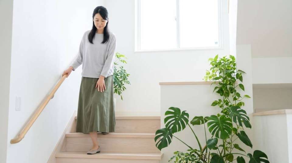 階段の手すりに手を添えてゆっくり下りる女性(イメージ)