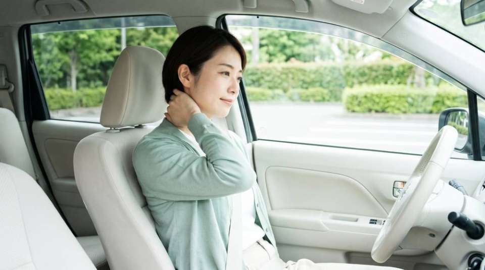 車の運転席で首の後ろに手を当てて様子を確かめる女性(イメージ)
